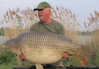 a man holding a large carp in front of a lake