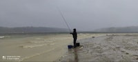 a man is standing on a beach with a fishing rod