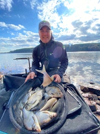 a man holding a net full of fish in front of a lake