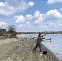 a man is standing on the shore with a fishing rod