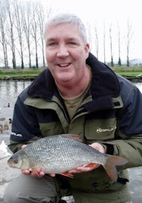 a man holding a fish in front of a pond