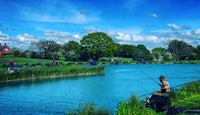 a man is fishing on a pond with a boat in the background